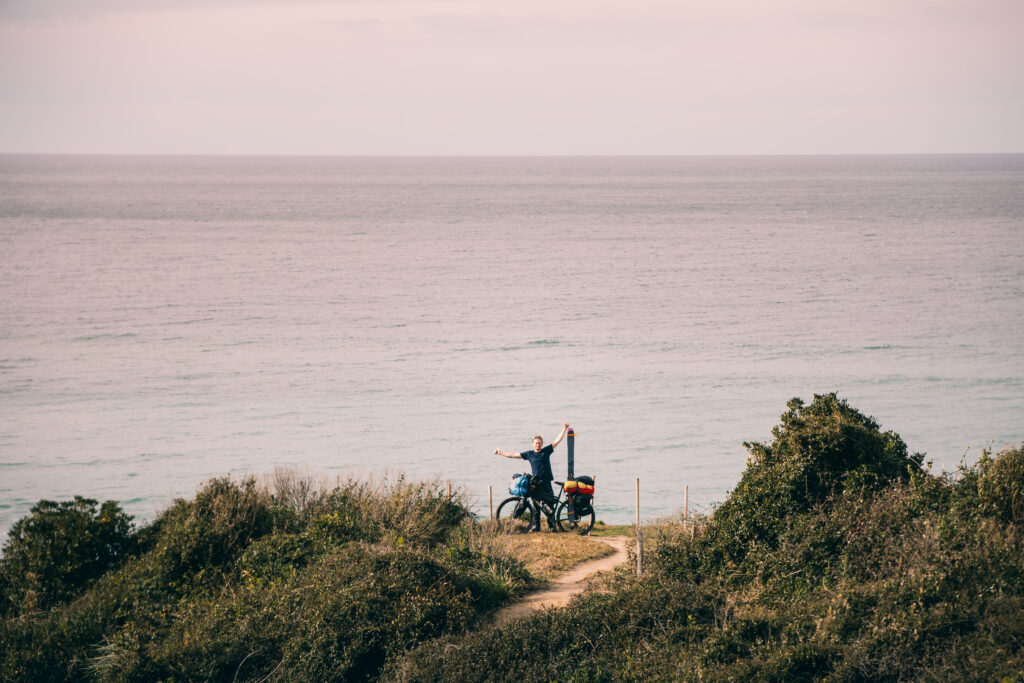 biker backpacking happy by the ocean with his bike