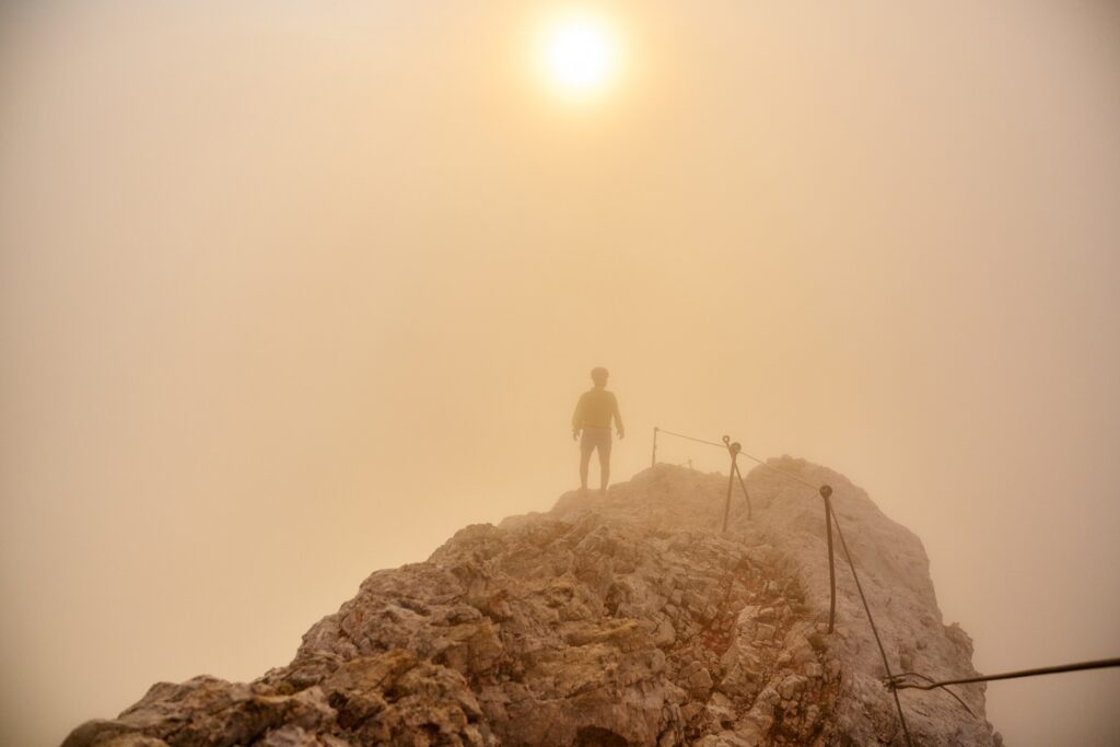 top of a mountain with a sun in the distance on a misty day