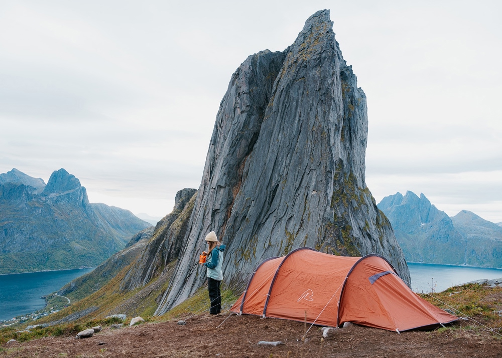 dame som spiser turmat utenfor teltet sitt med fin utsikt mot fjell 1000x714