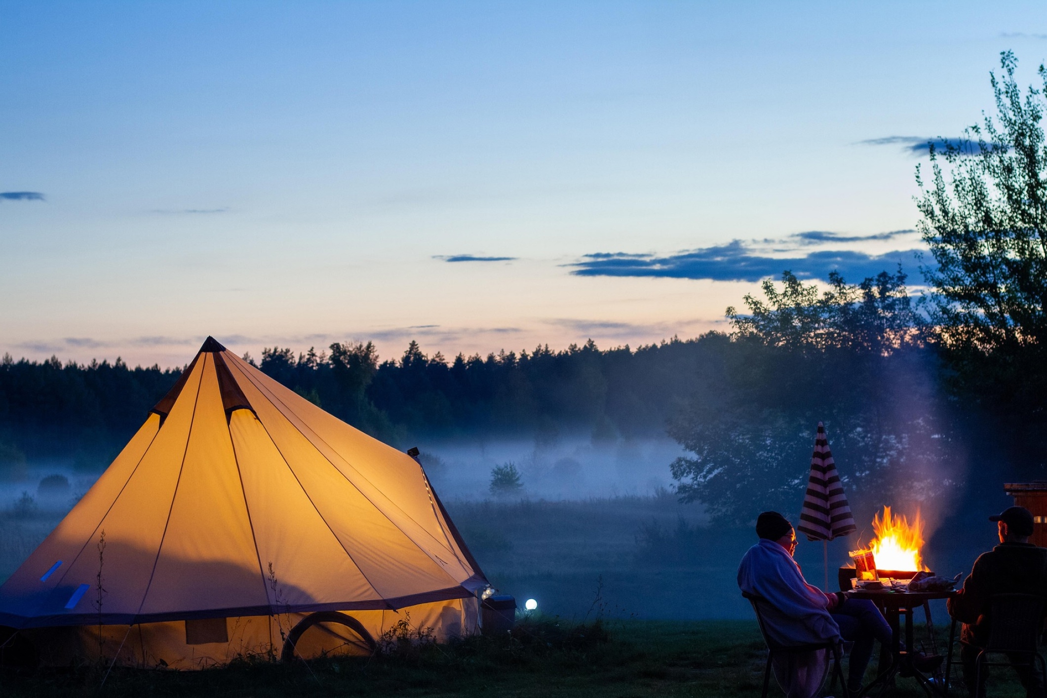 glamping tent in misty weather with two persons enjoying a fireplace