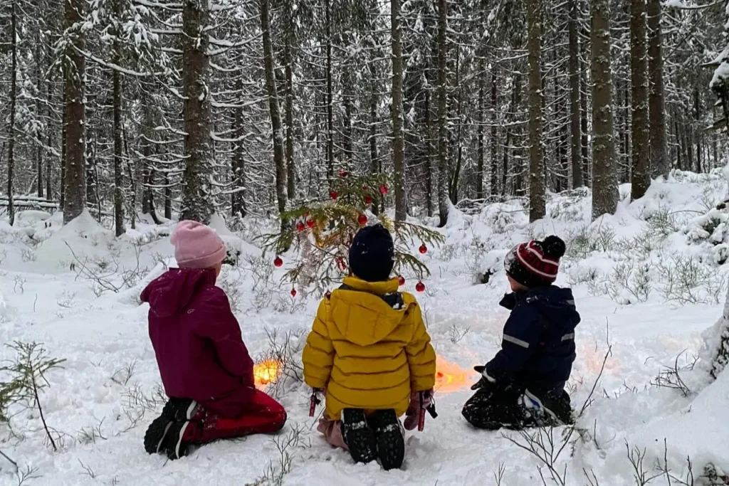 Three kids around a Christmas decorated tree out in the forest