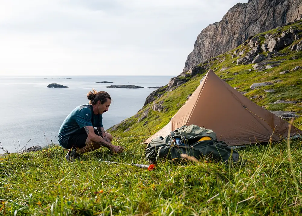 man setting up tent in the mountains in summer